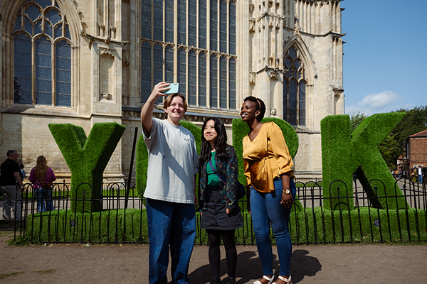Three students stood in front of the Minster in York taking a selfie